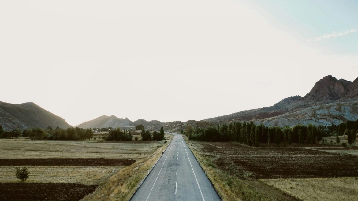 person-stands-in-middle-of-road-that-stretches-into-distance A person stands in the middle of a road that stretches into the distance, with mountains and a vast sky in the distance.