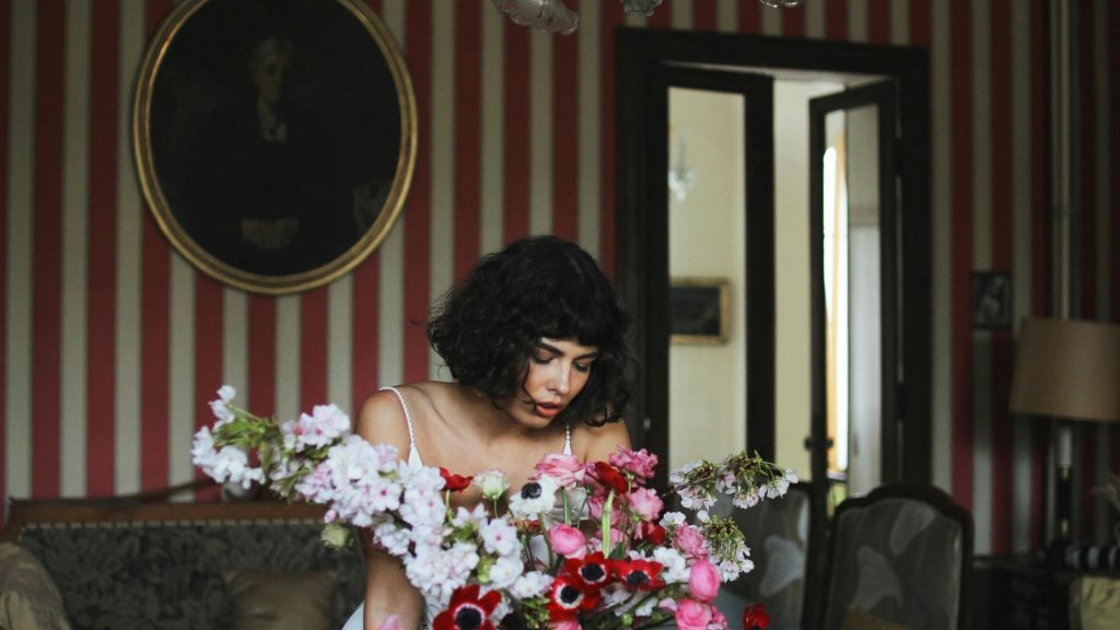 An elegant woman is smelling flowers in front of a gorgeous sofa